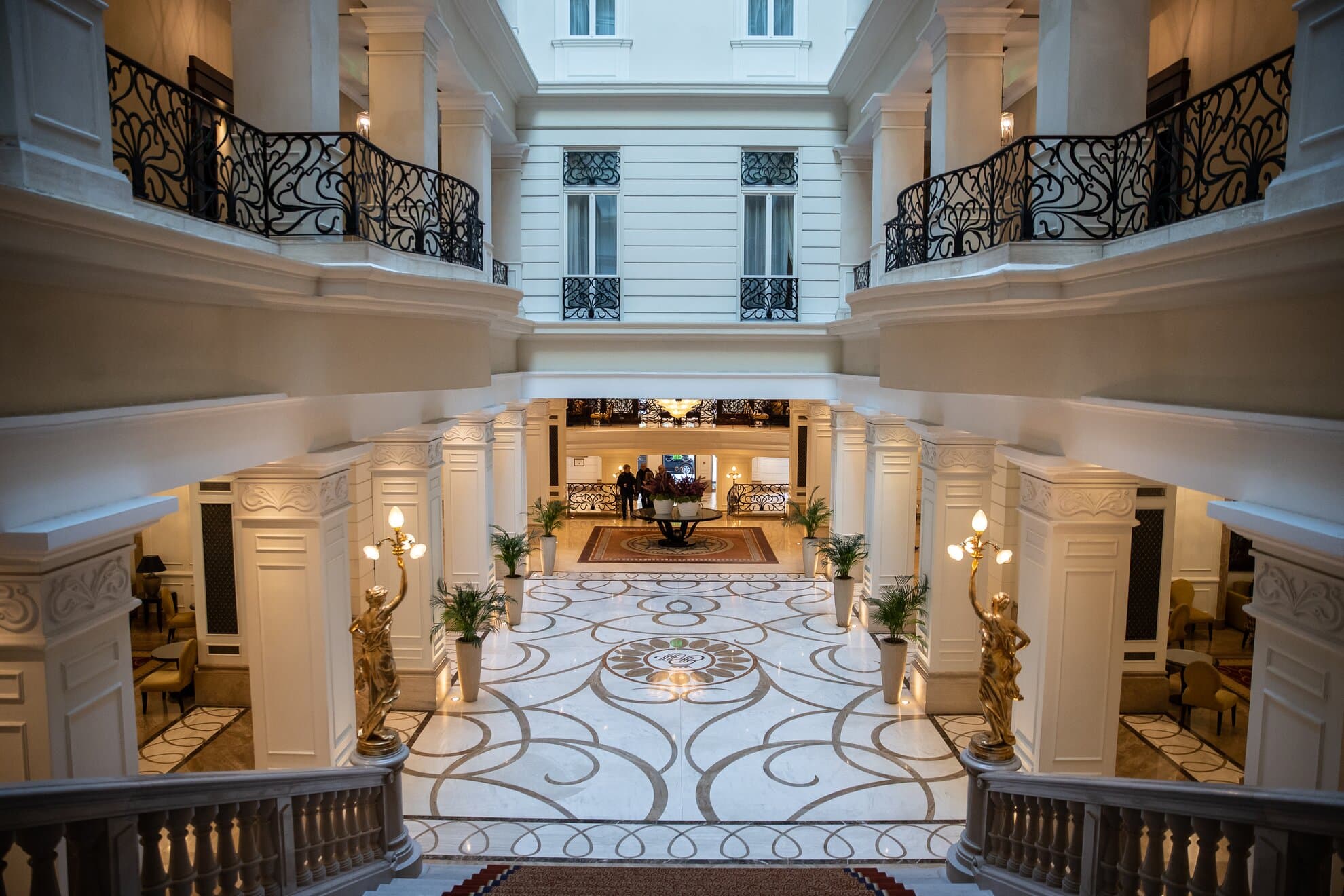 Atriumet og resepsjonsområdet i Corinthia Budapest med marmor, lyse vegger og smijernsdetaljer.